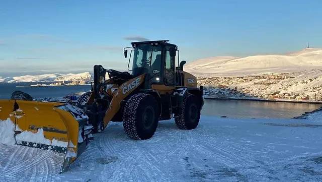 Hjullaster med snøplog i vinterlandskap ved kyst