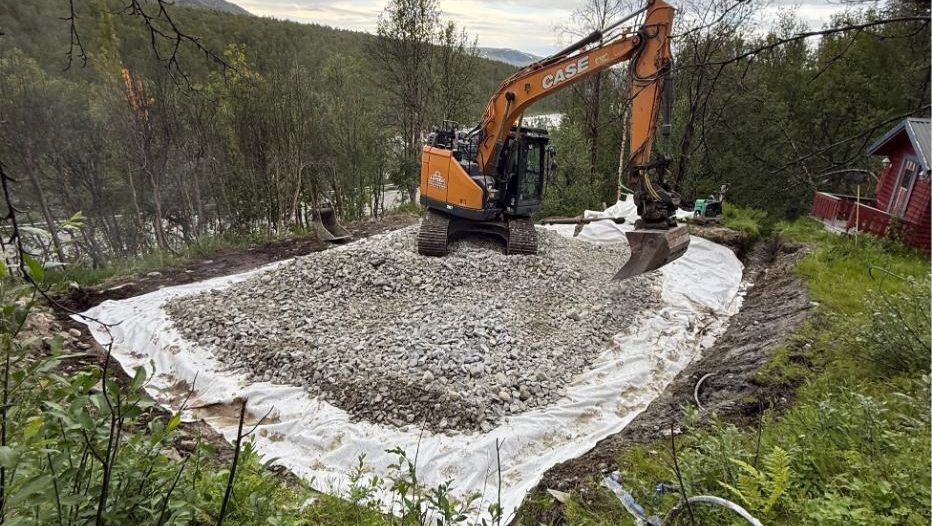 Gravemaskin planerer grusgrunn med duk i skogsterreng