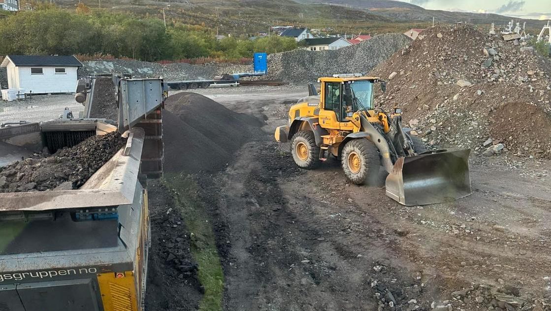 Hjullaster arbeider med masser på anleggsområde med grushauger